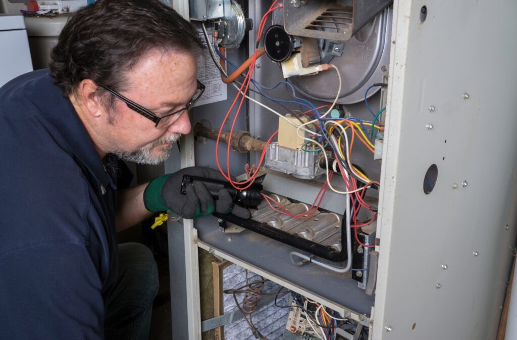 An old technician with spectacles is repairing an indoor Furnace system